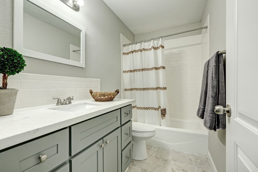 Modern bathroom with vanity, mirror, toilet, bathtub shower, and striped curtain in a remodeled home